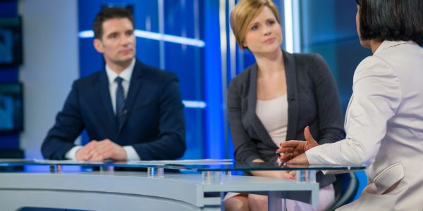 Trois personnes discutent dans un studio de télévision.