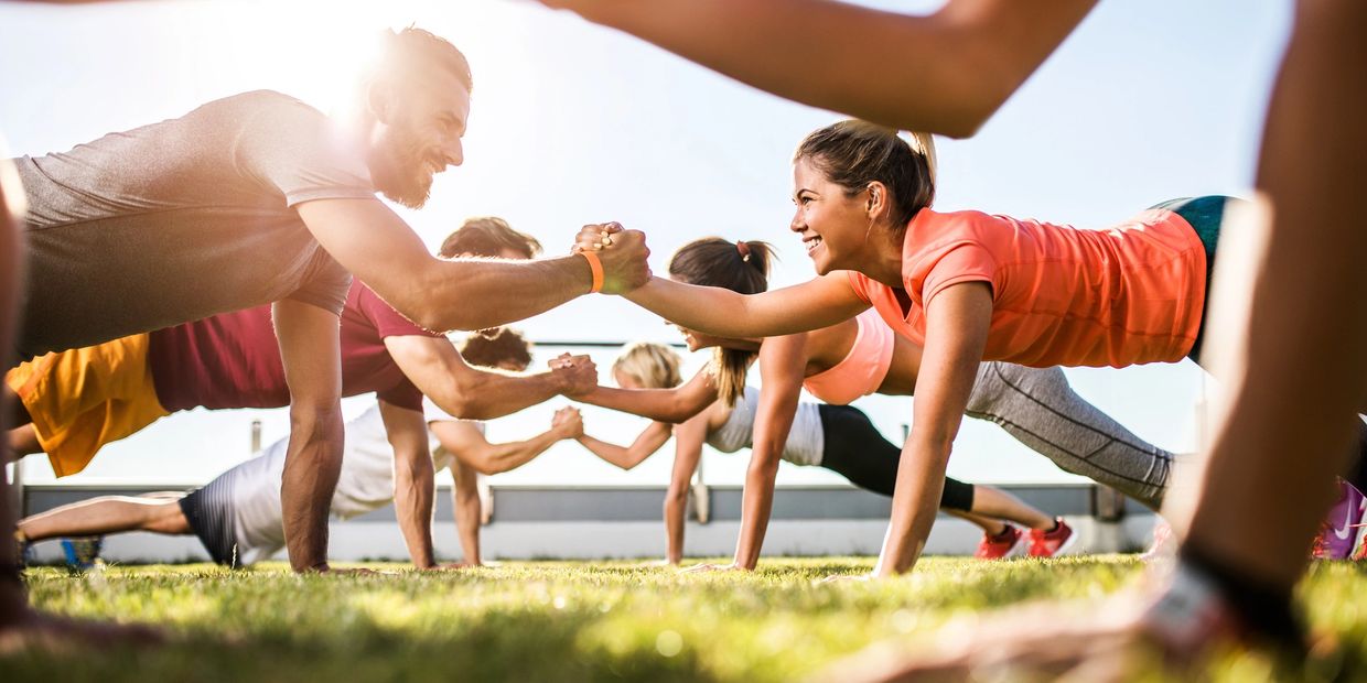 Group exercising outdoors, doing plank with handshakes.