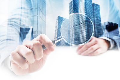 Businessman examining modern skyscrapers with a magnifying glass.