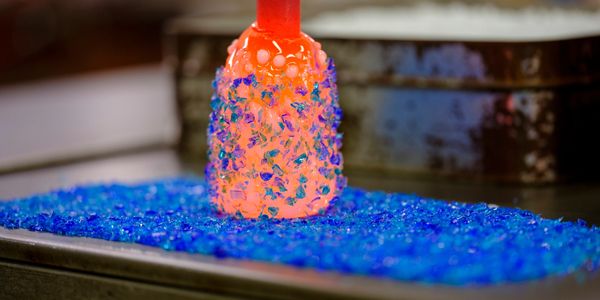 Hot glass being shaped by blue glass pieces.