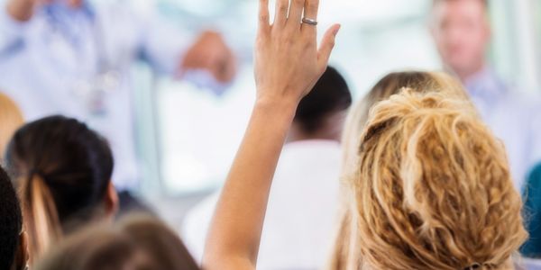 A person raises their hand to ask a question in a seminar or class.