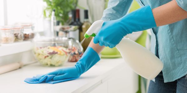 Person cleaning kitchen counter with gloves and spray bottle.