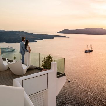 Couple overlooking calm sea at sunset from terrace.
