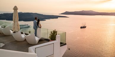 Couple in formal wear overlooking a scenic ocean sunset from a modern balcony.
