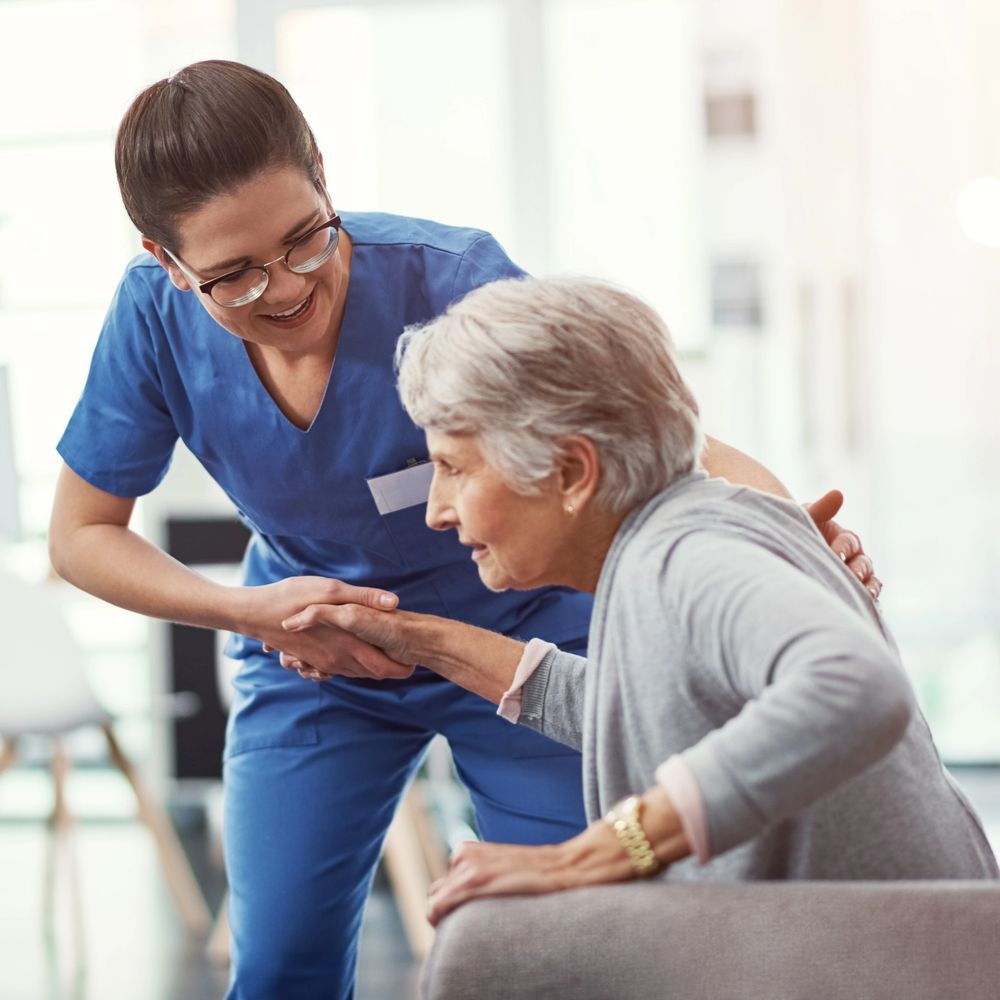 Nurse helping elderly woman stand up with a supportive smile.