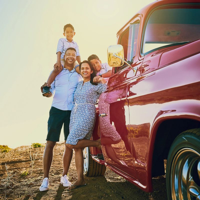 Shot of a cheerful family posing for a portrait together outside next to a red pickup truck