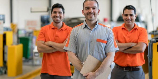 Three smiling mechanics in a workshop.