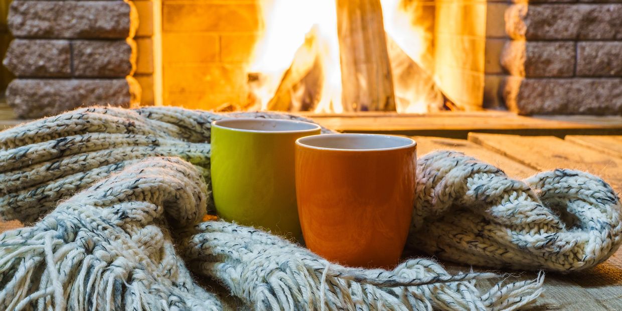 Two mugs wrapped in a cozy scarf by a warm fireplace.