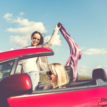 Two women enjoying a sunny day in a red convertible car.