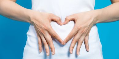 Person making a heart shape with hands on their stomach against a blue background.