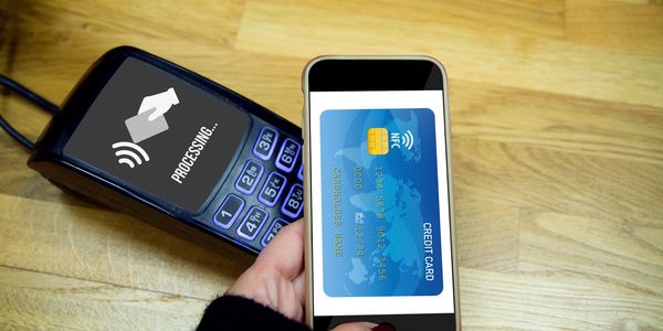 A person using a smartphone with a digital credit card to make a contactless payment on a POS terminal.