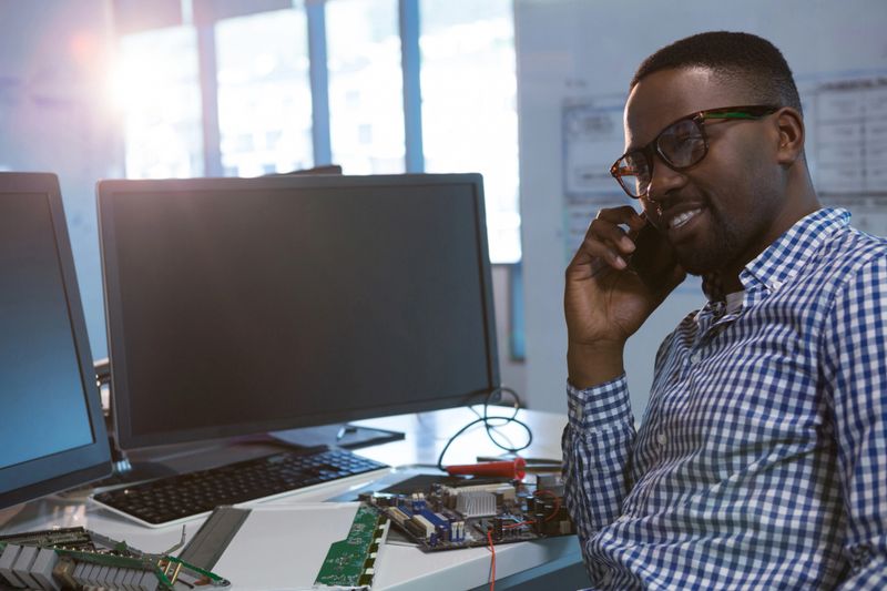 Computer engineer talking on mobile phone at desk in office