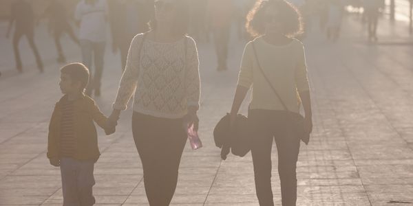 Two women and a child walking on a sunlit path, holding hands.