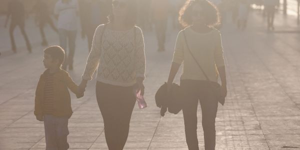 Two women and a child walking on a sunlit path, holding hands.
