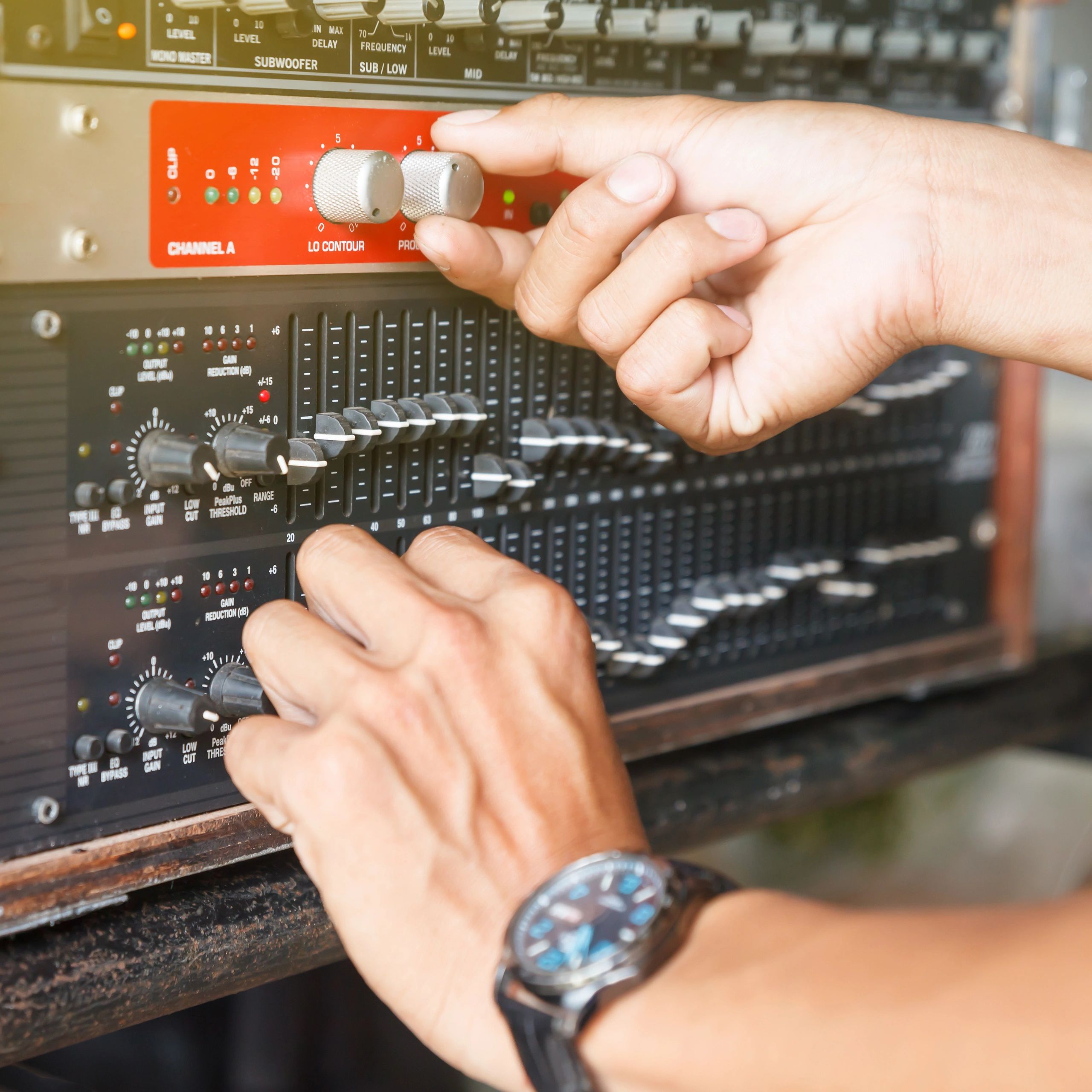 Hands adjusting audio mixer knobs and sliders.