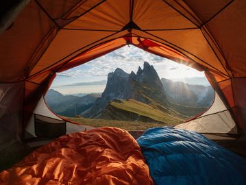 View of mountains from inside a tent with orange and blue sleeping bags.