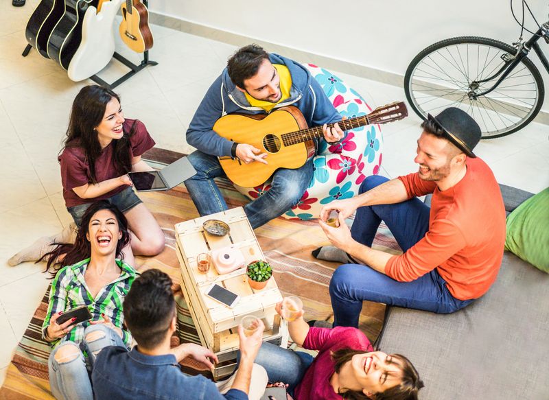 Trendy friends having fun in home living room - Happy young people enjoying time together playing music and drinking shots - Friendship and youth concept - Main focus on top left guys - Warm filter