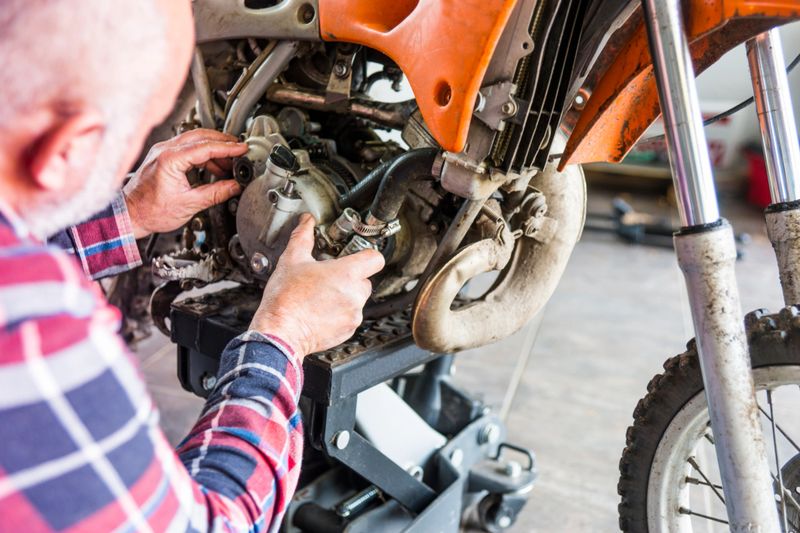 A mature man in his 50's working on a dirt bike in a garage.