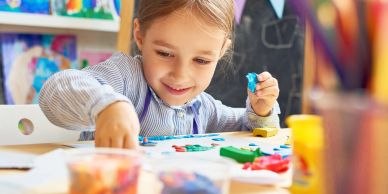 A young girl happily painting and creating art at a table.