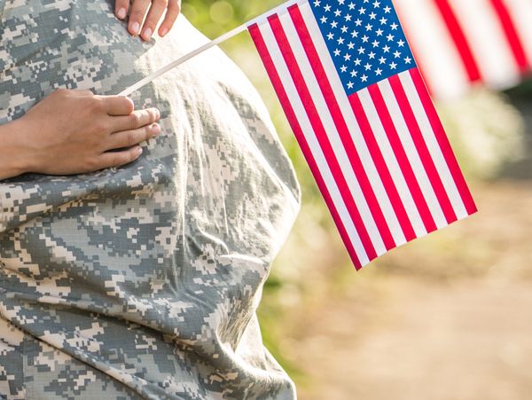 Pregnant soldier holding an American flag, symbolizing patriotism and family.