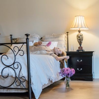 Woman lying on a bed with a vase of flowers on the floor.