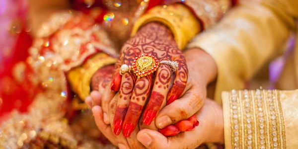 Close-up of a couple holding hands with intricate henna and jewelry.