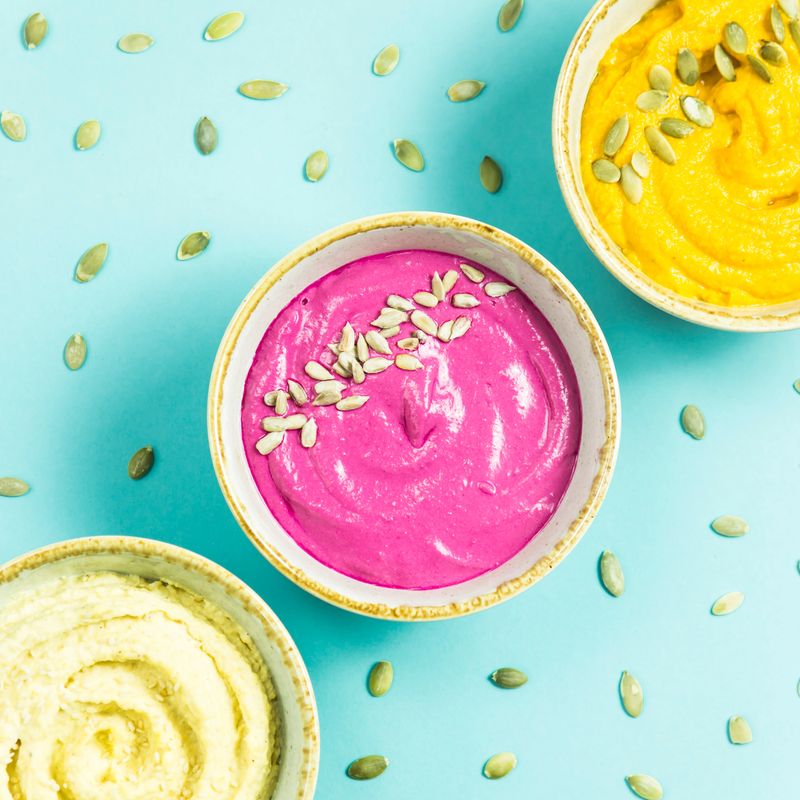 bright appetizers in the form of sauces on a blue background among pumpkin seeds. Hummus, carrot and beetroot sauces. Top view. Flat lay