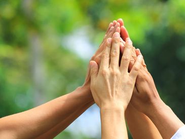 Four hands coming together in a high-five gesture outdoors.
