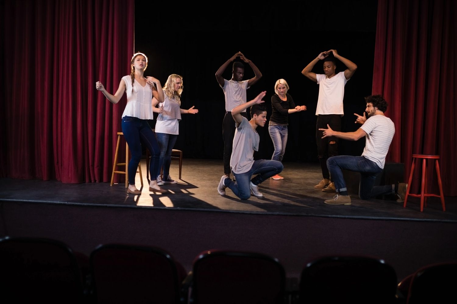 Group of actors rehearsing on stage with expressive gestures and poses.
