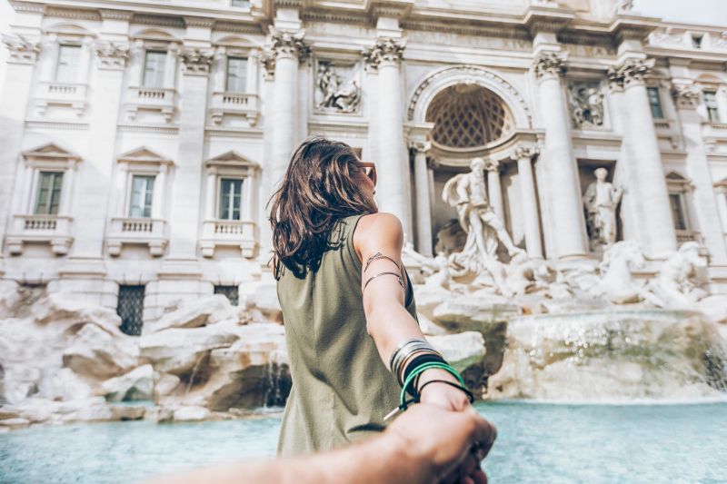 Young woman taking follow me picture in front of Trevi fountain in Rome