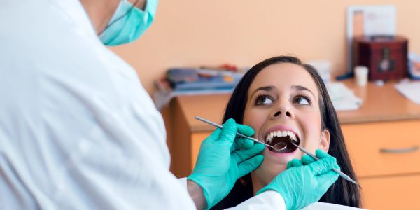 A dentist examining a female patient's teeth with dental tools.