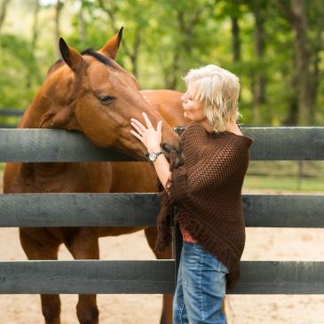 A young girl wearing a helmet gives a thumbs-up while standing next to a brown and white horse.