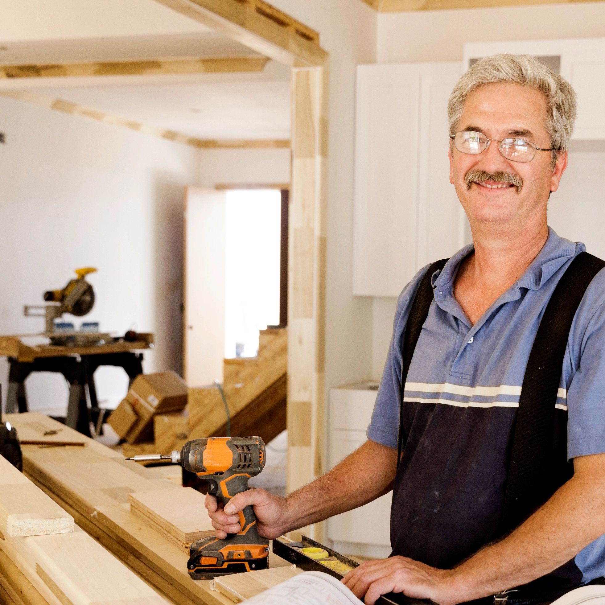 Smiling carpenter holding a power drill in a workshop under construction.