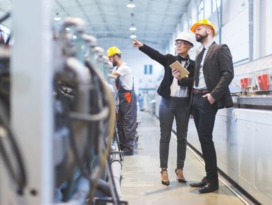 Engineers in safety helmets inspecting machinery in a factory setting.