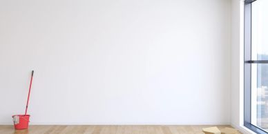 Empty room with white walls, wooden floor, mop, and bucket near a large window.