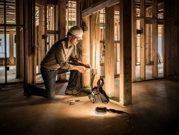 Construction worker kneeling and working with tools inside a wooden-framed building.