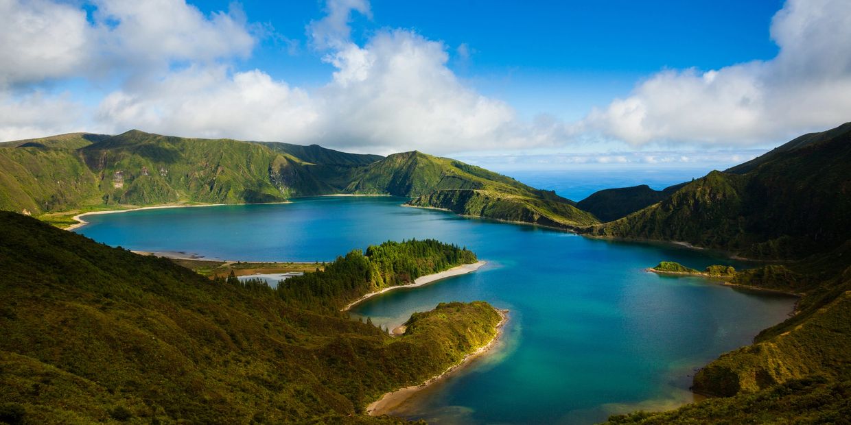 Scenic lake surrounded by lush green mountains under a blue sky.