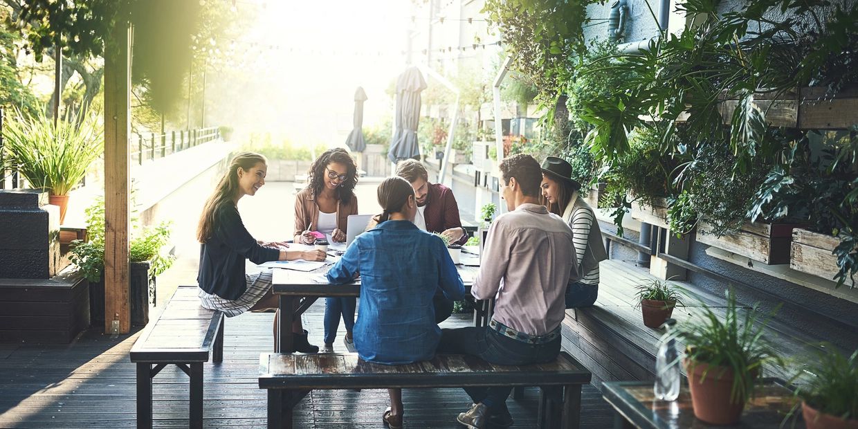 A diverse group of professionals engaged in a collaborative discussion in an outdoor garden setting.