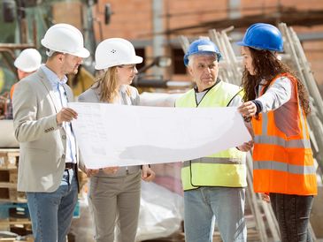 Four construction professionals reviewing blueprints at a building site.