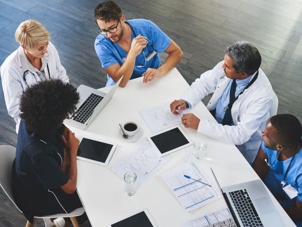 Medical team discussing patient data around a table with laptops and tablets.