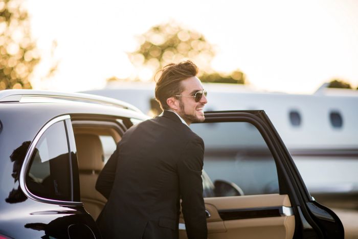 Man in sunglasses smiling while getting out of a car.