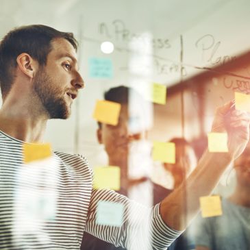 Man brainstorming ideas on sticky notes on a glass wall in an office.