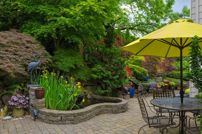 Home backyard hardscape and lush plants landscaping with garden furniture on paver brick patio
