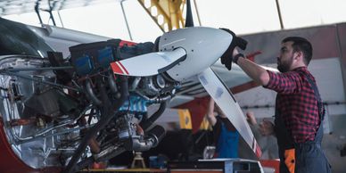 Mechanic working on airplane propeller in hangar.