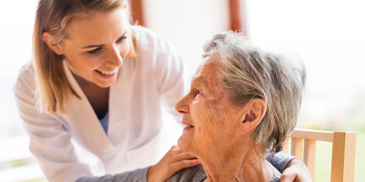 A caregiver smiles at an elderly woman with warmth.