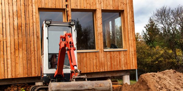 Excavator working in front of a wooden house under construction.