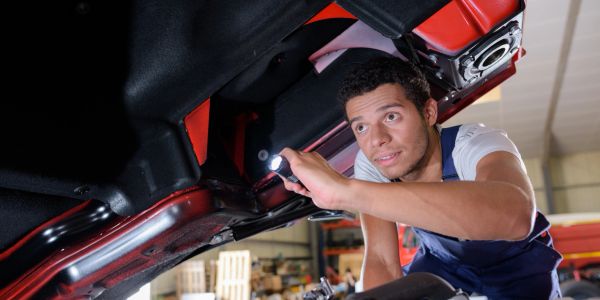 Mechanic inspecting car underside with a flashlight.