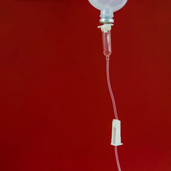 IV drip bag with tubing against a red background.