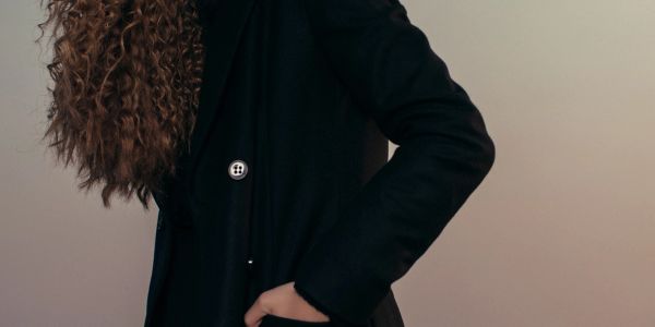 Person in black coat with curly hair.