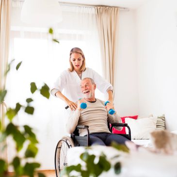 Caregiver assisting elderly man in wheelchair with light dumbbells.
